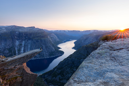 Sunset on the Norwegian fjord Trolltunga. Couple hiker sitting on a cliff above a lake, Trolltunga, Norway Concept of adventure, freedom and extreme lifestyle