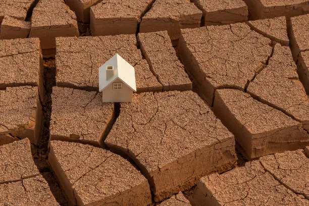 Photo of A wooden symbolic house stands on the cracked red clay in the desert
