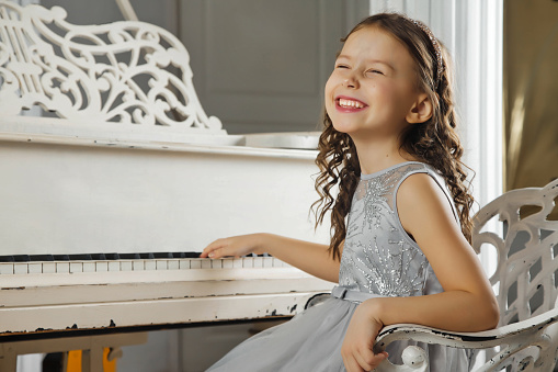 Cute little girl in blue dress playing an old antique grand piano