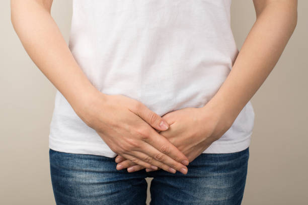 foto de primer plano recortada de una mujer joven con camiseta blanca y jeans sosteniendo sus manos en la entrepierna sobre un fondo gris aislado - thrush fotografías e imágenes de stock