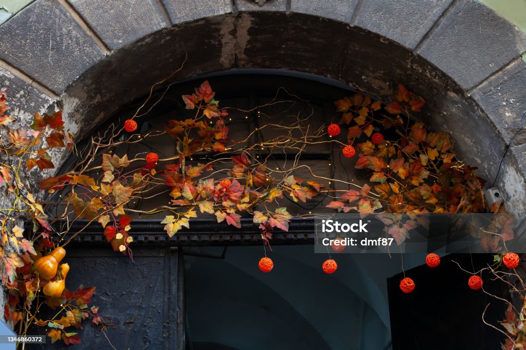 Entrance of house decorated with autumn leaves and orange wicker balls for Thanksgiving holiday. House entrance decorated with leaves and orange wicker balls for Thanksgiving holiday. Fall festive artificial red leaf, lights garland on doorway for Halloween Arch - Architectural Feature Stock Photo