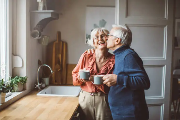 Senior couple for Christmas at home. They are standing in front of kitchen window and drinking tea or coffee.