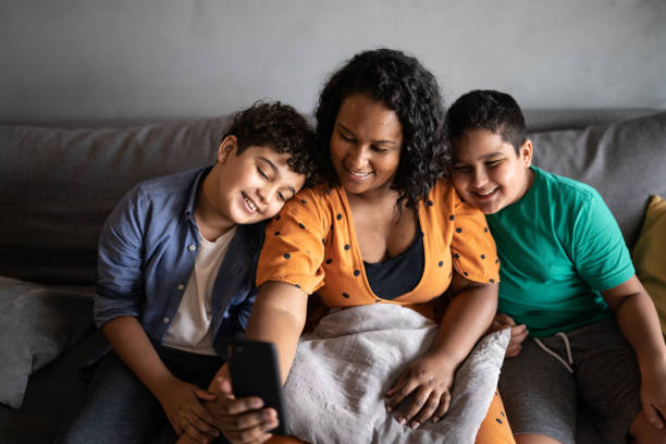 Mother and son using mobile phone at home Mother and son taking selfies or talking on a video call on the smartphone at home family dependency mother family with two children stock pictures, royalty-free photos & images