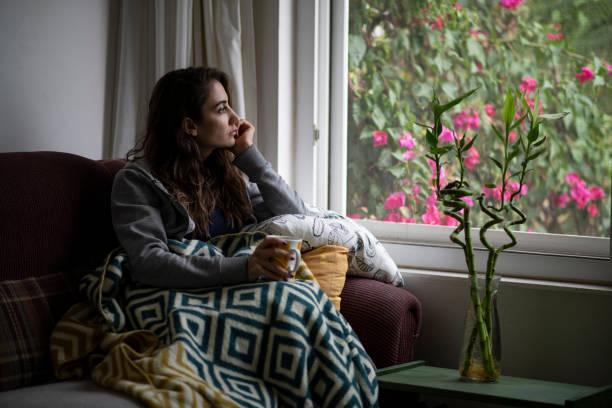 donna depressa seduta alla finestra - solo una donna giovane foto e immagini stock