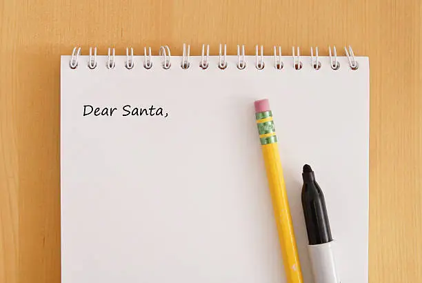 Caption Dear Santa on note pad with pencil and black marker on wooden desk