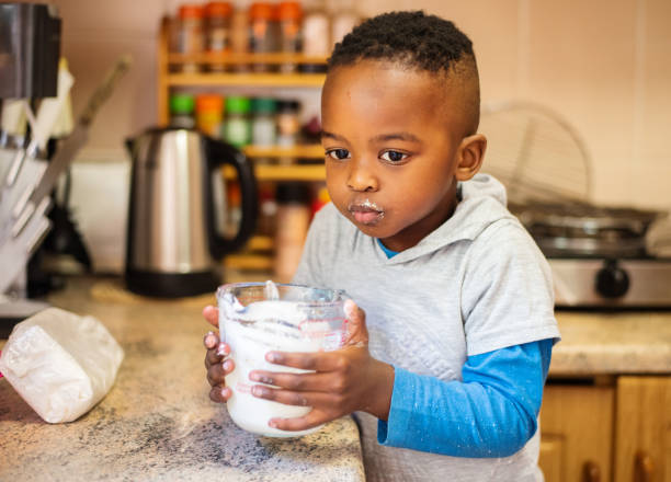 istock Cute little boy drinking from a measuring cup at a kitchen counter 1346885082