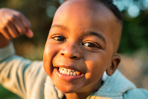 Close-up portrait of a cute little African boy laughing while playing outside on a sunny afternoon
