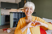 istock Portrait of a senior woman at home showing a heart-shaped symbol 1346887540