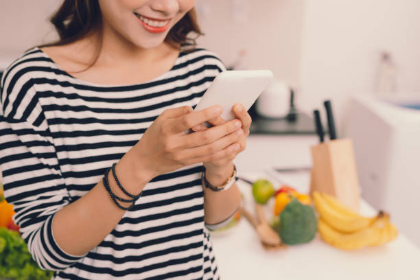 istock Attractive young girl busy using mobile phone or checking updates in smartphone while wearing apron in kitchen 1346889336