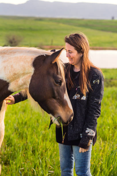istock Smiling farmer standing with her horse in a farm pasture 1346890141