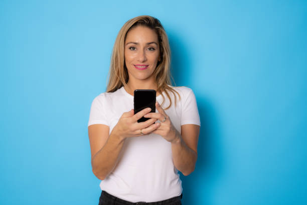 istock Beautiful woman using mobile phone isolated over blue background. 1346896233