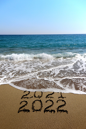 New year 2022 and old year 2021 written on sandy beach with waves
