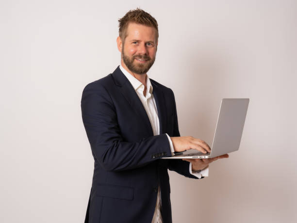 istock Young business man standing with laptop. Handsome guy holding open notebook in his hand and work on it. Information, technology concept. 1346902333