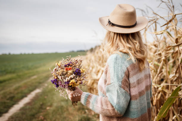 kobieta z dzianinowym swetrem i kapeluszem trzymająca bukiet suszonych kwiatów na zewnątrz - autumn clothing corn crop fashion zdjęcia i obrazy z banku zdjęć