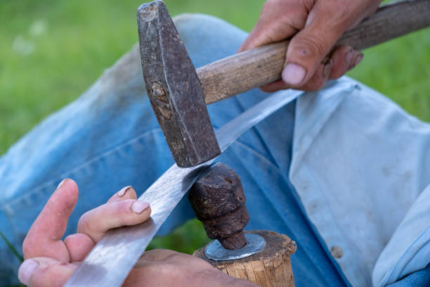 istock Hone a scythe blade with hammer 1346906242