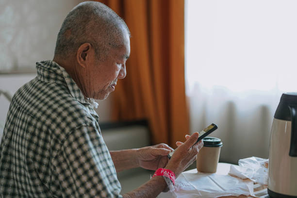 asian chinese senior male patient looking at his smart phone in hospital ward sitting on bed asian chinese senior male patient looking at his smart phone in hospital ward sitting on bed tracheotomy tubing stock pictures, royalty-free photos & images