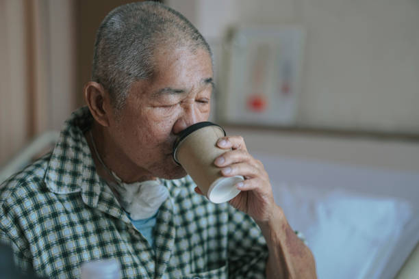 asian chinese senior male patient drinking coffee in hospital ward sitting on bed asian chinese senior male patient drinking coffee in hospital ward sitting on bed tracheotomy tubing stock pictures, royalty-free photos & images