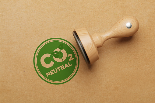 Green CO2 Neutral stamp sitting next to wooden stamp over brown paper background. Horizontal composition with copy space. Sustainability and renewable energy concept.