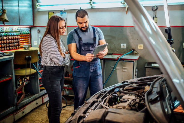 Auto mechanic and female customer in garage Woman talking to a mechanic fixing her car and looking at results on a tablet computer auto repair shop mechanic digital tablet customer stock pictures, royalty-free photos & images