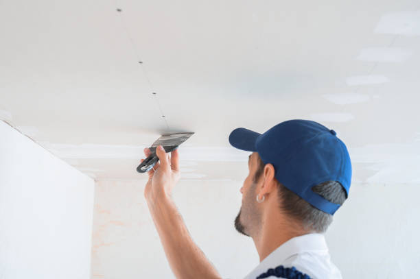 istock A master in uniform puts putty on the caps of self-tapping screws for fixing plasterboard sheets on the ceiling. 1346922061