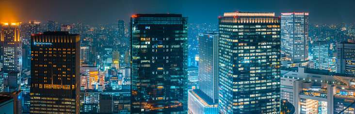 Aerial panoramic view across the futuristic neon night skyscraper skyline of Osaka’s crowded cityscape, Japan.