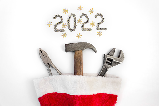 Flat composition with construction tools in santa claus hat on on a white background with 2022 lined with screw nuts. The concept of New Year and Christmas in the construction industry. Top view. Flat lay.