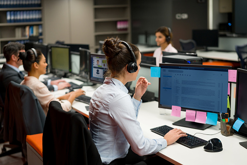 Group of people working as customer service representatives at a call center using headsets while talking on the phone. **DESIGN ON SCREEN BELONGS TO US**