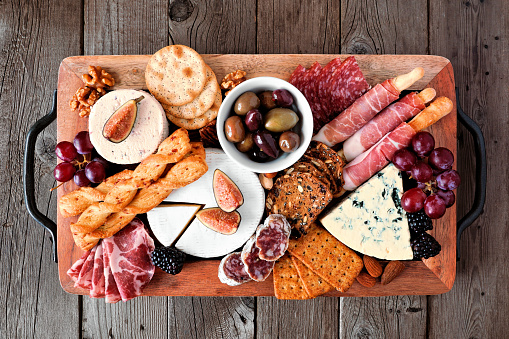 Charcuterie tray of a variety of meats, cheeses and appetizers. Top view on a dark wood background.