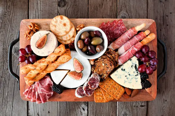 Charcuterie tray of a variety of meats, cheeses and appetizers. Top view on a dark wood background.