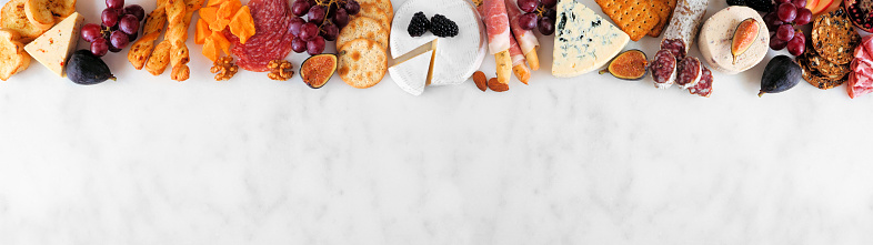 Variety of cheese and meat appetizers. Above view top border on a white marble banner background with copy space.
