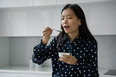 若いアジアの女性は、キッチンで朝食に新鮮なヨーグルトを食べます
