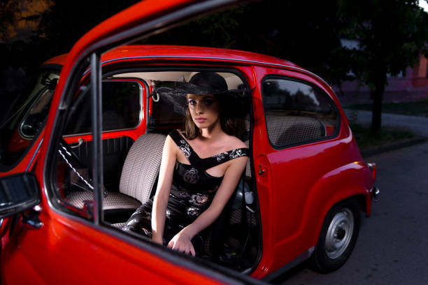 A fashion model posing besides a red car. Vintage look in sun set.