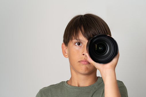 A serious teenager in a green T-shirt on a green background looks through the camera lens.