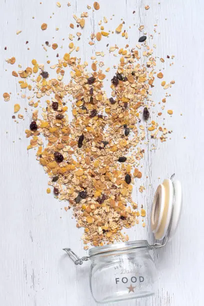 flying muesli, muesli spilled out of a glass jar. Healthy breakfast with wholegrain cereals on a white wooden background, flat lay