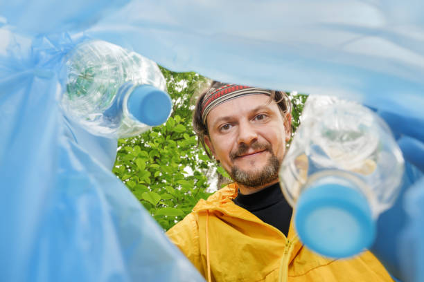 istock Volunteer collecting litter picking up trash plastic bottle in garbage bag. Picking up garbage plastic bag. Volunteer cleaning park view from inside a trash bag. Altruistic man collect garbage forest 1346945820