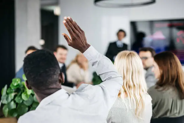 Photo of Young businessman raising his hand at a meeting