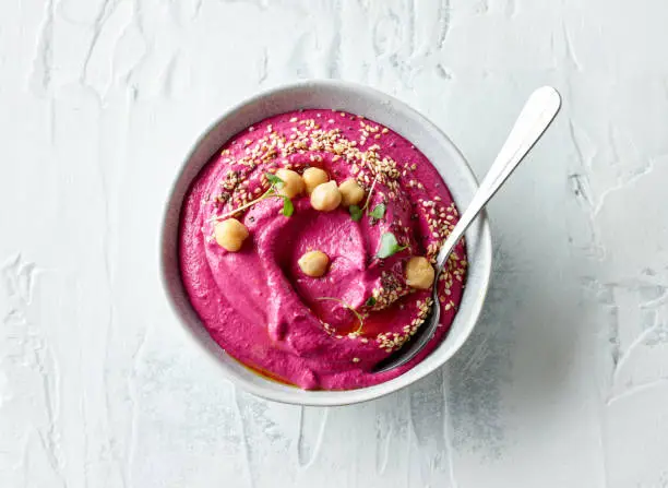 bowl of beetroot hummus on light kitchen table, top view