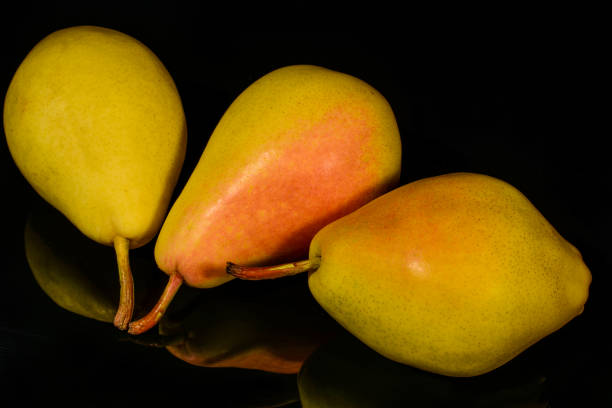 ripe yellow pear fruit, with reflection in black surface, isolated on black