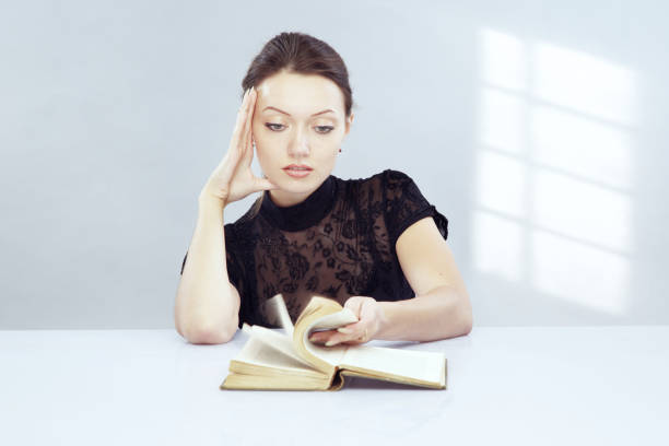 istock Young woman searching for chapter in a  textbook while turning pages. Sunlight shadow from window on the wall 1346953151