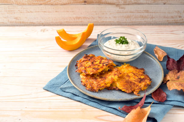 buñuelos o panqueques de patata de calabaza con una salsa de crema de cuajada en un plato azul y una mesa de madera, comida vegetariana de otoño, espacio de copia, enfoque seleccionado - patata picada y frita fotografías e imágenes de stock