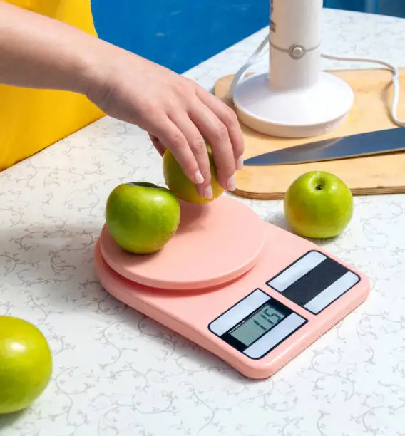 Weighing apples on kitchen scales, hand holding an apple. Selective focus.
