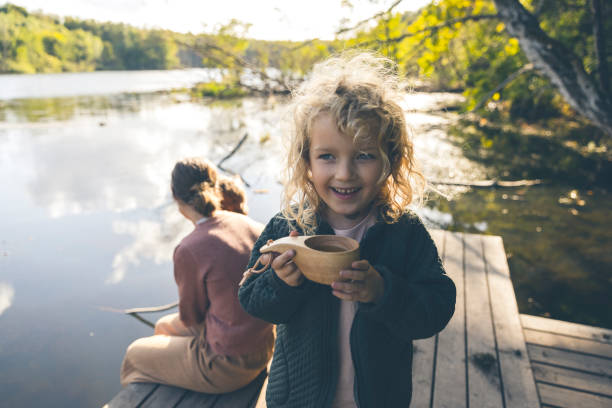 Mother relaxing outdoors at a lake with her cute kids: a boy and girl  with blond hair having fun outdoors in nature