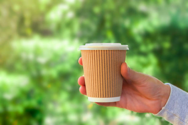 istock Hand holding eco-friendly paper coffee cup on green nature background 1346962008