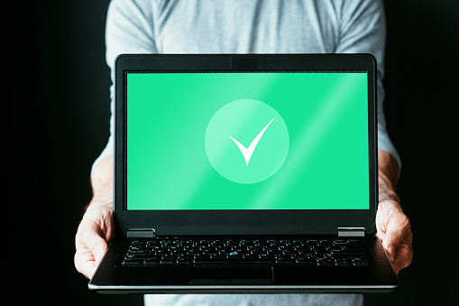 Antivirus protection. Access safety. Malware cybersecurity. Personal data security. Unrecognizable man holding notebook with green checkmark on screen isolated on black free space.