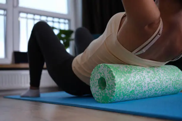 Woman doing foam roller exercises to relieve back pain. Posture correction with a roller concept
