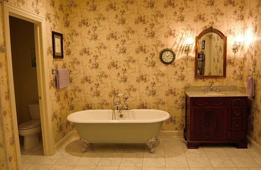 A clawfoot bathtub, sink and mirror in a wallpapered bathroom