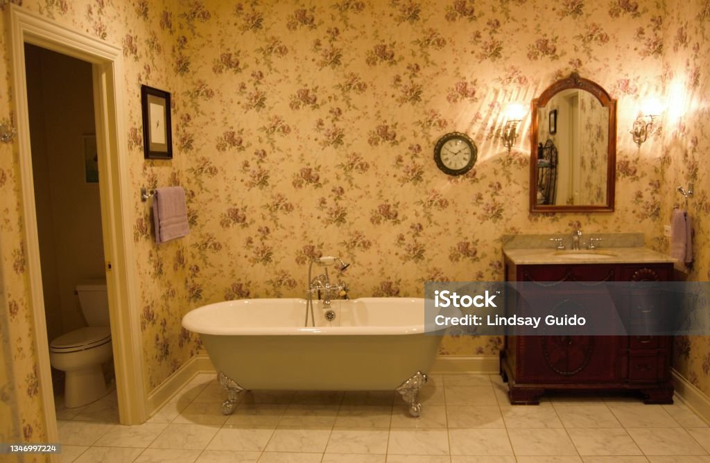 Take a Bath A clawfoot bathtub, sink and mirror in a wallpapered bathroom Old-fashioned Stock Photo