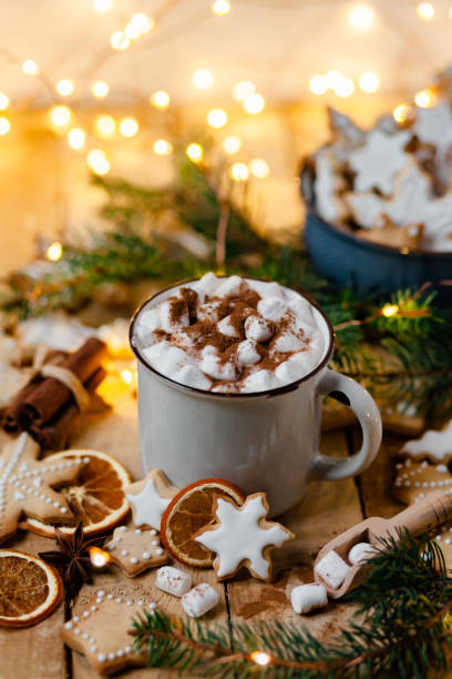 istock Winter hot drink: white mug with hot chocolate with marshmallow and cinnamon. Cozy home atmosphere, festive holiday mood. Rustic style, wooden background. Homemade gingerbread cookies, dry orange 1346998166