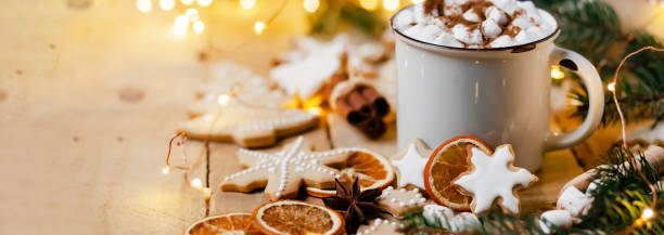 istock Winter hot drink: white mug with hot chocolate with marshmallow and cinnamon. Cozy home atmosphere, festive holiday mood. Rustic style, wooden background. Homemade gingerbread cookies, dry orange 1346999169
