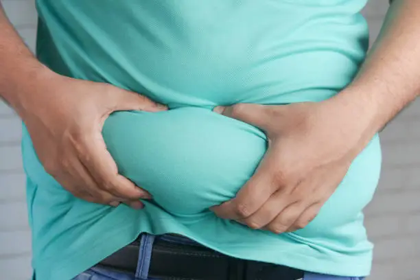 Photo of man's hand holding excessive belly fat, overweight concept